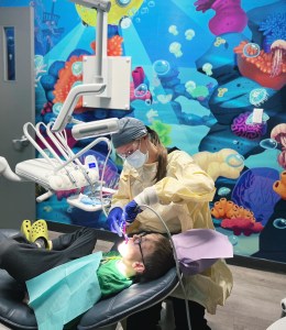 Dental Assistant located at Oasis Family Dental polishing and applying fluoride to young patient teeth